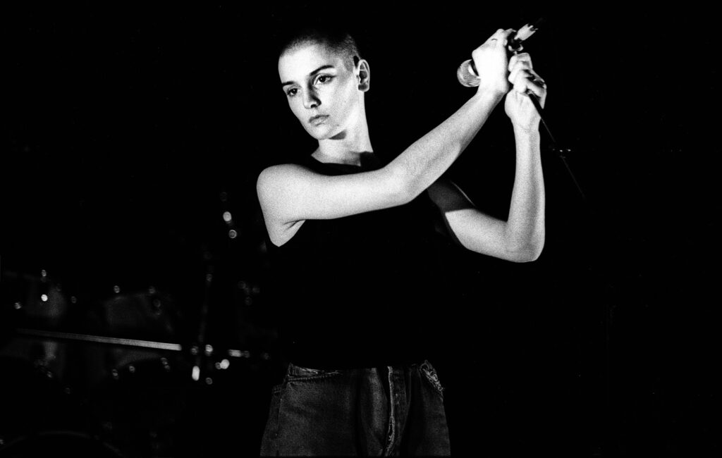 a black and white photograph of Sinead O'Connor performing live on stage in 1988