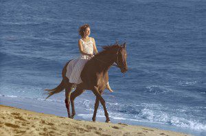 Carole King riding horse on beach for 