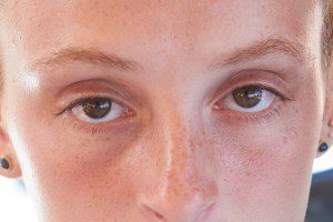 red-headed teenage girl with long straight hair brown eyes close up of girl looking at camera no emotion face to face with camera daytime daylight sunny image frame cuts off the top of her head sitting outside girl is looking up at the camera